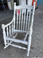 White wooden rocking chair frame shown from front angle on tiled floor, missing seat base and cushion.