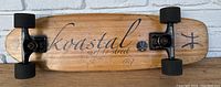 Full view of the skateboard deck showing Koastal logo, wooden deck, black trucks, and wheels with visible scratches and wear.