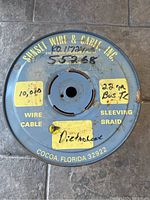 Top view of blue metal spool with yellow labels showing wire specifications and company name.