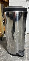 Front view of tall stainless steel kitchen garbage can with dent on the body and black foot pedal.