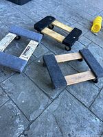Three small wooden furniture dollies on a stone pavement, showing carpet and padded ends, caster wheels, and wood frames.