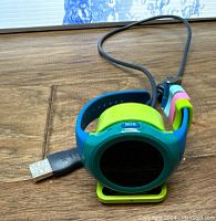 Preowned Timex FamilyConnect smartwatch for kids with round touchscreen and colorful adjustable band. The watch is placed on a wooden surface with an attached USB charging cable next to it.