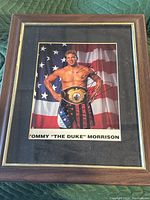 Frontal view of the framed and matted autographed photo of Tommy Morrison with the American flag in the background and championship belt on his waist.