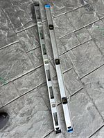 Two aluminum carpenter levels lying parallel on a textured stone surface showing their full length with multiple bubble vials and end caps in blue and black.