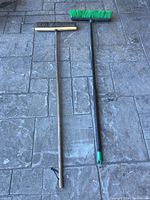 Photo showing two pushbrooms laid side by side on stone pavement, highlighting overall length and handle material contrast.