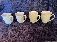 Four white ceramic Denby mugs, view from front showing shape and handles.