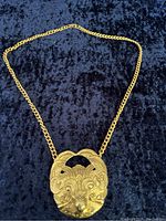 Full view of the gold toned chain necklace with lion medallion on black fabric background