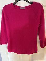 Full view of pink cashmere sweater hanging on black hanger showing the front and overall color and fit.