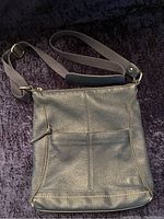 Blue pebbled leather purse with adjustable canvas strap and gold-tone hardware against black background.