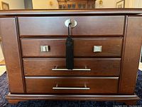 Front view showing wooden jewelry chest with four drawers, metal handles, lock with tassel key