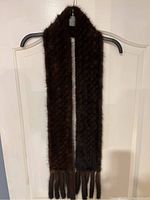 Full view of the brown knitted mink scarf hanging on a hanger, showing its length and tassels.