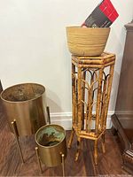 Two gold metal planters with three-legged stands, wicker plant stand, wooden lined planter bowl with red box on top.