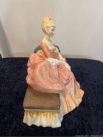 Side view of Royal Doulton figurine showing seated woman in pink dress on cushioned bench.