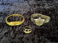 Three items on black velvet: gold-tone enamel floral bracelet watch, sterling silver ring with onyx and mother of pearl inlays, and Timex stainless steel wristwatch