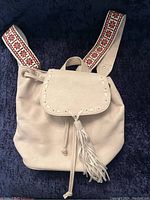 Front view of cream knapsack purse showing flap with metal studs and embroidered shoulder straps