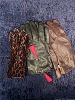 Top view of three pairs of gloves: leopard print stretch gloves, black leather gloves with red tassels, brown leather gloves.