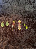 Three pairs of earrings displayed on dark textured fabric: green teardrop earrings, multicolor beaded dangle earrings, and small green drop earrings.