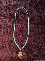 Full view of turquoise bead necklace with sterling silver pendant on dark fabric background.