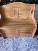 Front view of wooden toy chest with hinged lid open showing storage space, featuring natural wood grain and panel design.