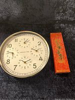 World time clock with five dials and decorative chopsticks box on black background.