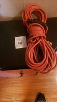 Two coiled orange extension cords tied with black straps on a black surface with a sticker number 123 visible.