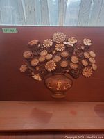 Full view of copper art mounted on a wooden backboard showing flowers in a vase.
