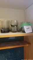 Display of 10 smoky gray Libbey glasses in various sizes on a shelf. Glasses are stacked and need cleaning.