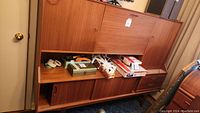Mid-century modern wooden wall unit cabinet closed with miscellaneous items stored on middle shelf.