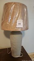 Full view of terra cotta lamp with new plastic covered lampshade showing natural beige color and texture.
