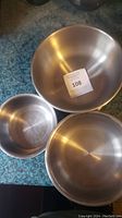 Three stainless steel mixing bowls of varying sizes arranged on a countertop, showing reflective brushed metal finish.
