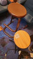 Photo showing brown leather seat stool with tubular metal base and footrest next to wooden round seat stool with black tripod base