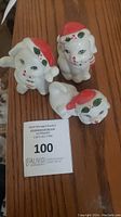 Three vintage white ceramic dog figurines with red and green Christmas hats and scarves on wooden surface.