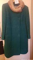 Full front view of green wool coat with tan fur collar on hanger.