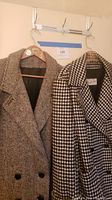 Photo showing two vintage wool coats hanging side by side on hangers on a wall hook.