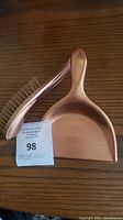 Full view of the copper crumb brush and matching dustpan on a wood surface.