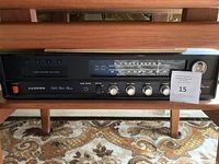 Front view of vintage Lloyd's stereo receiver showing the radio tuner, control knobs for volume, bass, treble, and balance, and power switch. Unit is placed on a wooden shelf above a carpeted floor.