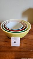 Set of 4 nested Pyrex mixing bowls in yellow, green, red, and blue with white interiors, stacked inside each other.