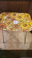 Front view of vintage metal folding TV table with yellow and orange sunflower tin top on thin metal legs