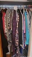 Closet rod with a variety of vintage women's apparel featuring jackets, dresses, and sweaters with mixed patterns including houndstooth and floral.