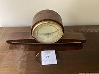 Front view of vintage wooden mantle clock showing circular face with glass and brass rim on rectangular wooden base.