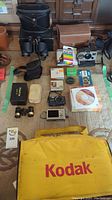 Image showing Kodak yellow camera bag and cameras, binoculars, film and accessories laid out on carpeted floor.
