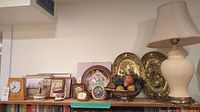 Shelf with clocks, lamp, wall hangings, and decorative elements