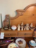 Photo showing corn husk dolls, brass candle holders and porcelain incense burner on wooden dresser with carved backboard.