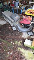 Side view of Honda push lawn mower with attached grass catcher and two gas cans nearby