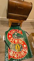 Wooden case for sewing machine with 'SINGER' on front and green apron with large Singer Sewing Machines logo and vintage illustration