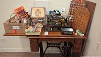 Full view of Singer sewing table with sewing supplies arranged on top including vintage Singer sewing machine, spools of thread, scissors, and boxes of sewing notions.