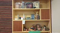 Shelf with assorted souvenirs encompassing glassware, ceramic and pottery figurines, plus small decorative objects.