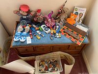 Full assortment of toys displayed on a wooden chest including dolls, game boards, toy cars, marbles, and plush toys.