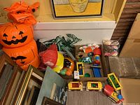 View of the assortment showing inflatable pumpkin stack, green claw hand decorations, various small toys in a box, and framed art.