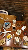 Overhead view of table with multiple ashtrays, assorted lighters, model airplane and ceramic tile